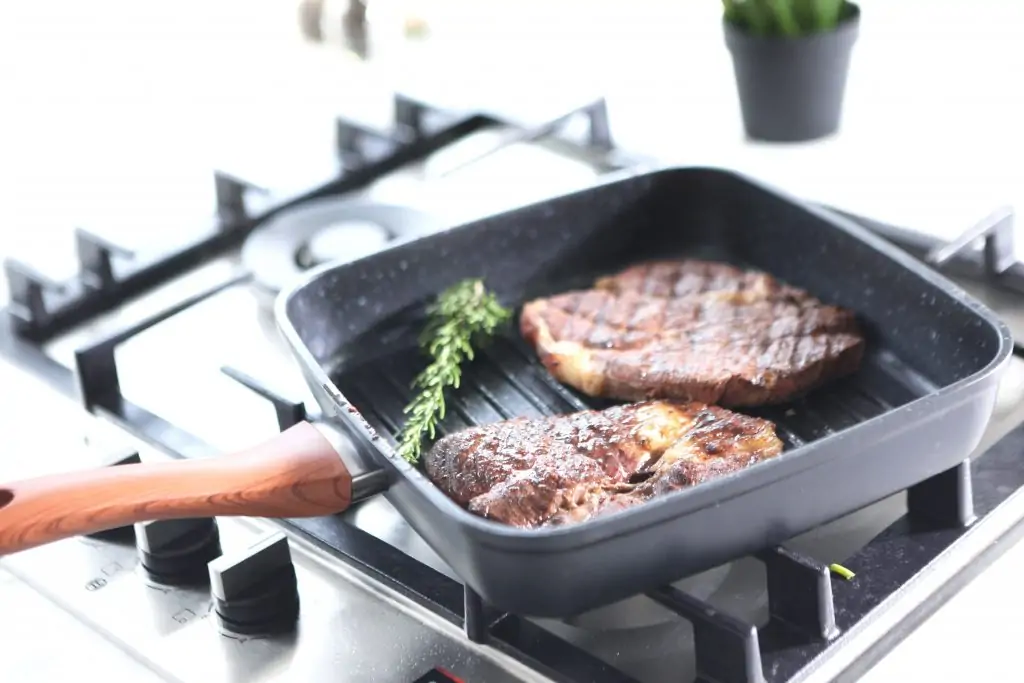 griddle pan with 2 steaks being grilled on a gas hob