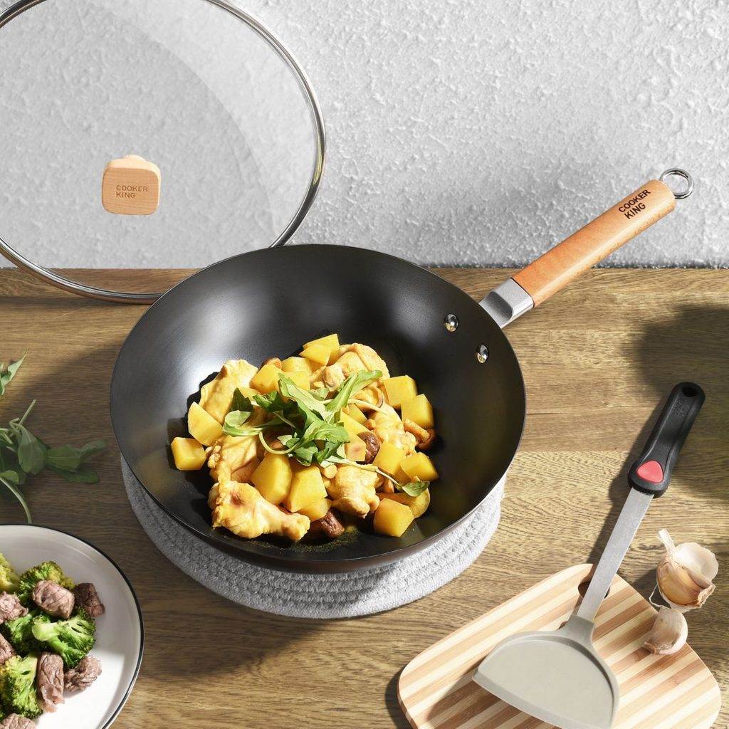 wok containing chicken and potatoes resting on a benchtop with various kitchen items alongside
