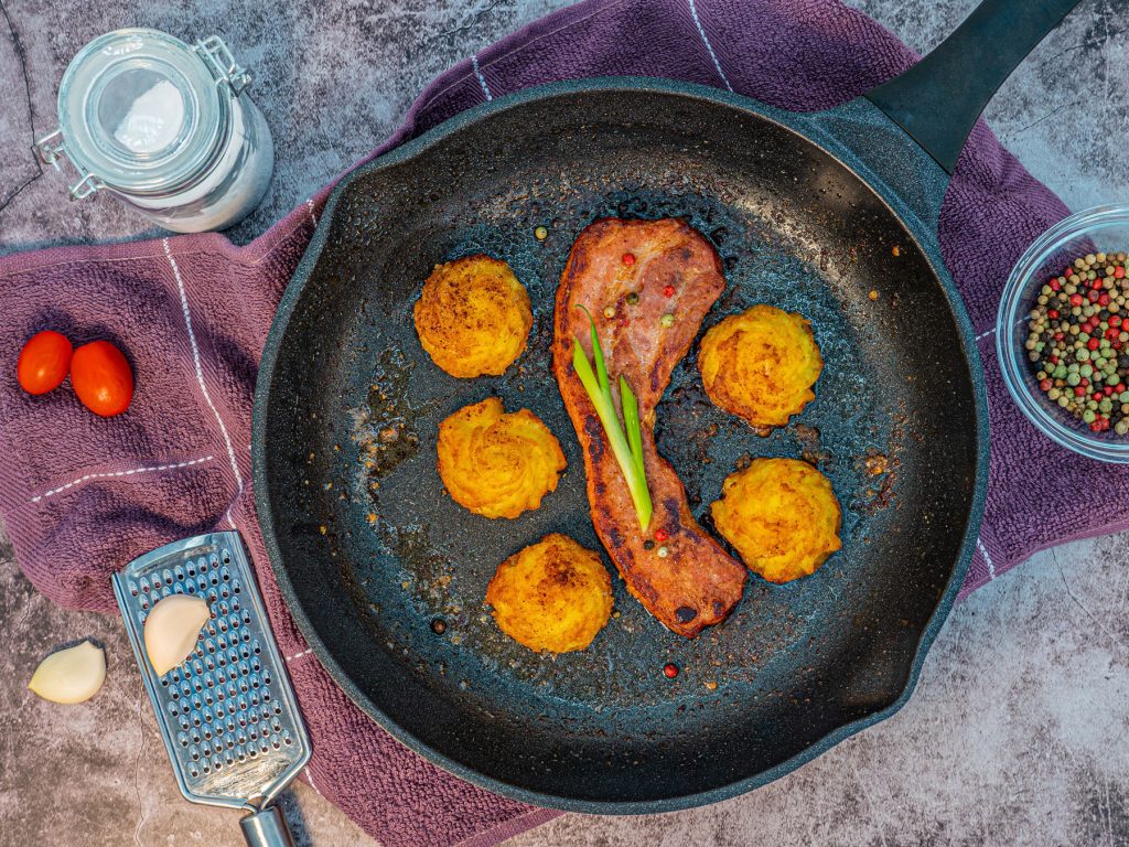 frying pan with bacon and fritters resting on a purple cloth