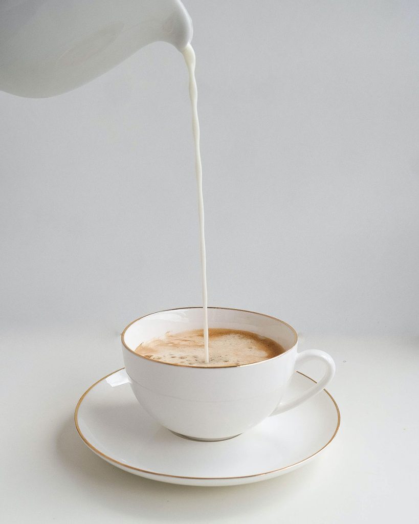 white jug pouring milk into a coffee cup from a great height!
