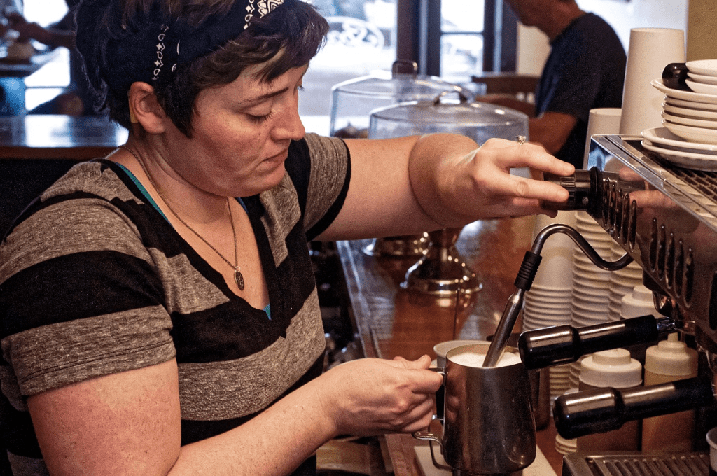 female barista frothing milk in a busy cafe