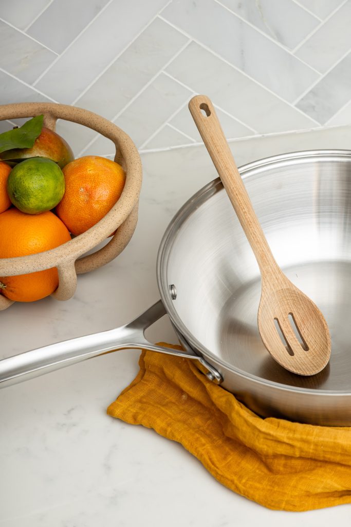 saucepan with a wooden spoon next to a bowl of fruit
