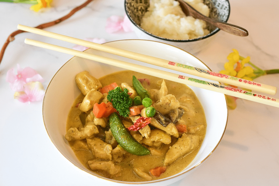 chopsticks resting on a white bowl with chicken curry, 