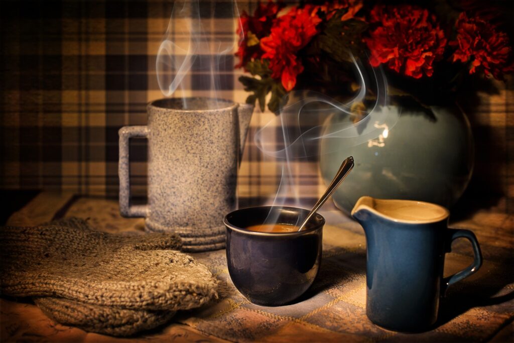 steaming hot mugs of tea alongside a milk jug and a vase of red flowers in the background