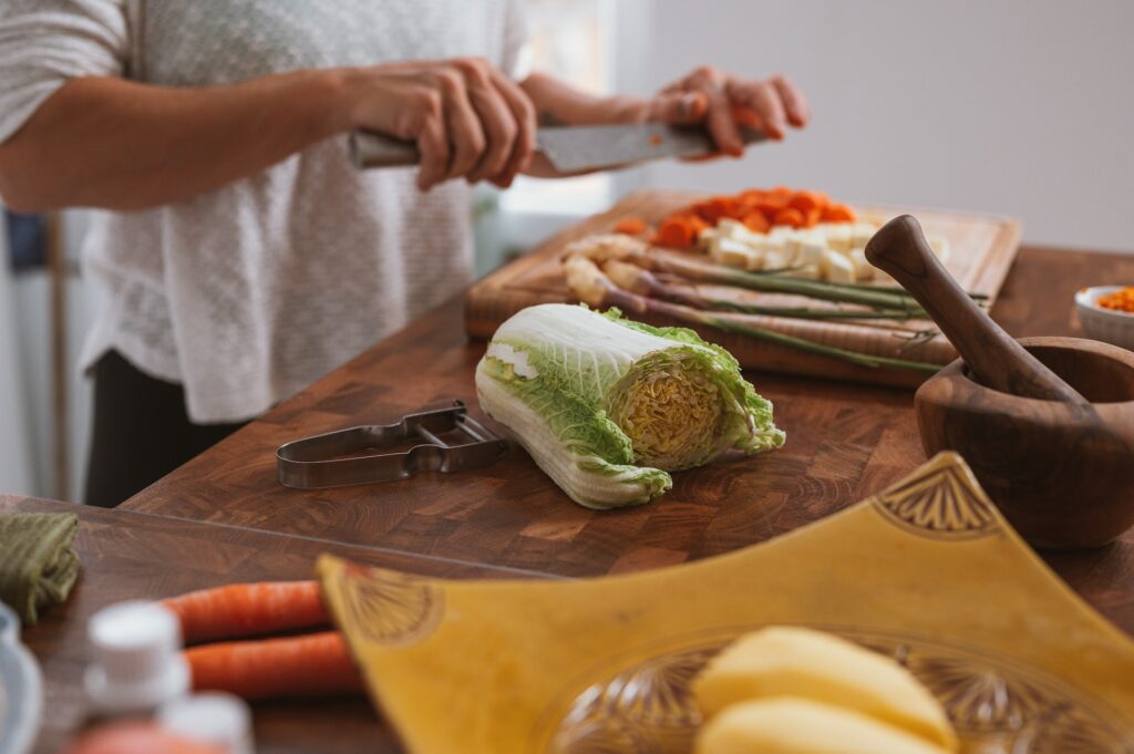 person holding a knife above a food that has been chopped on a chopping board