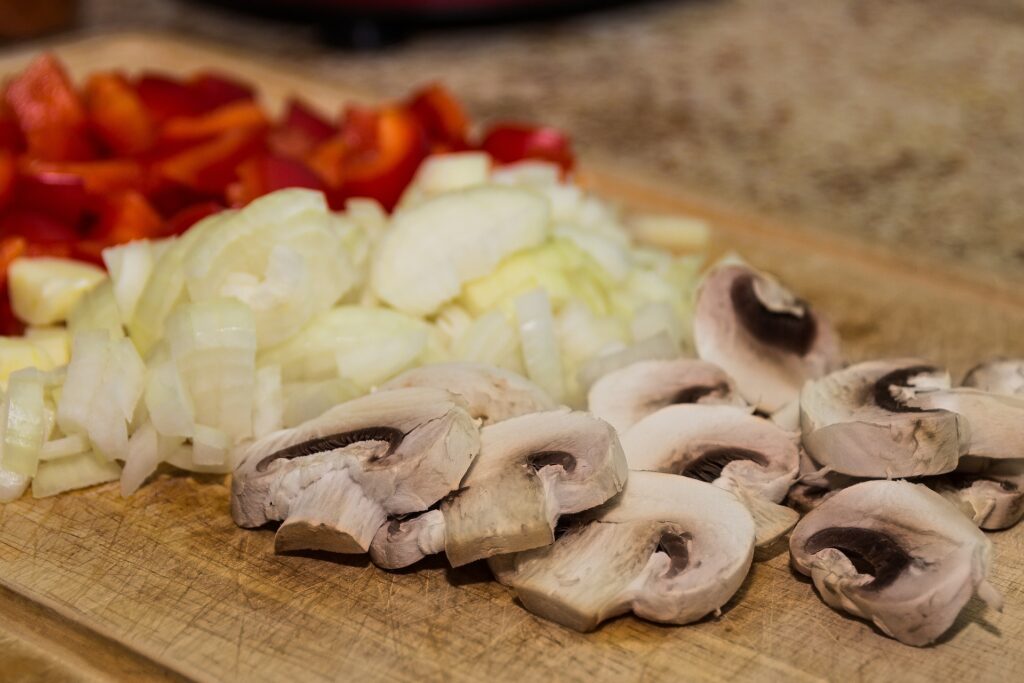 chopped capsicum, onion and mushroom on a wooden chopping board