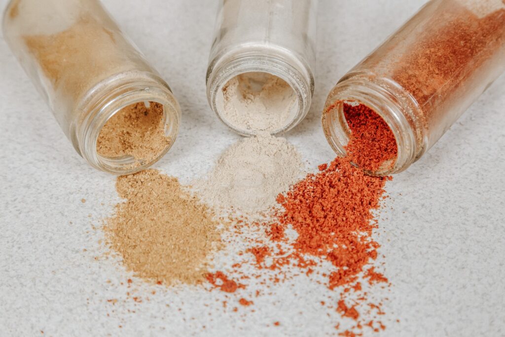 3 glass spice bottles spilling their colourful contents onto a white surface