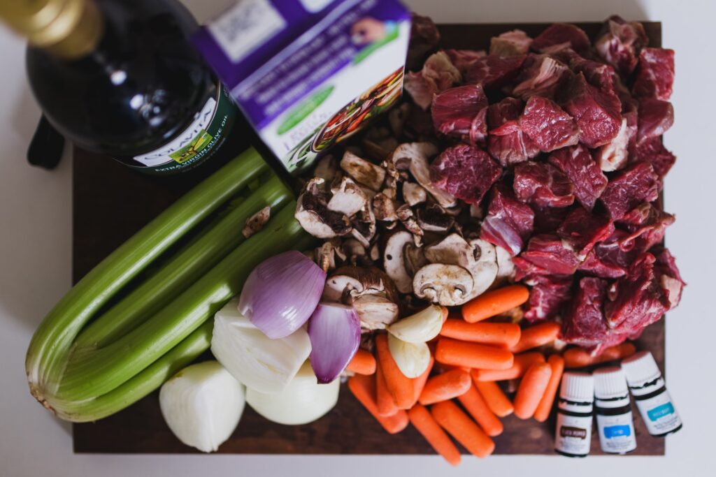 celery bunch, onions, carrots, spices, beef cut into cubes, mushrooms and olive oil on a dark board